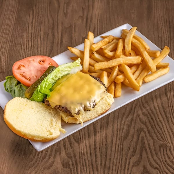 A Bushwick Diner cheeseburger with fries, lettuce, tomato, and a pickle on a white plate.